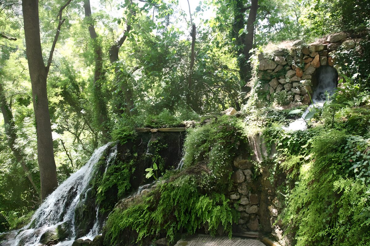 Muur van keien met een kleine waterval begroeid met diverse planten