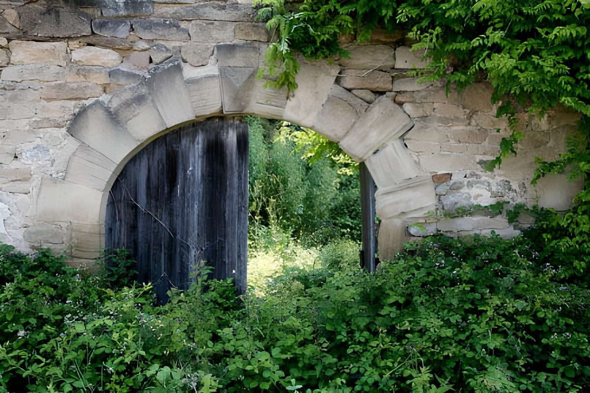 Deur in poort met muur en groene begroeiing 1