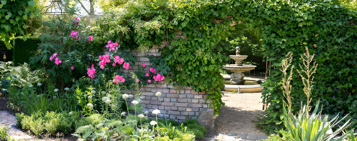 Muur begroeid met rozen en poort met uitzicht op een fontein.