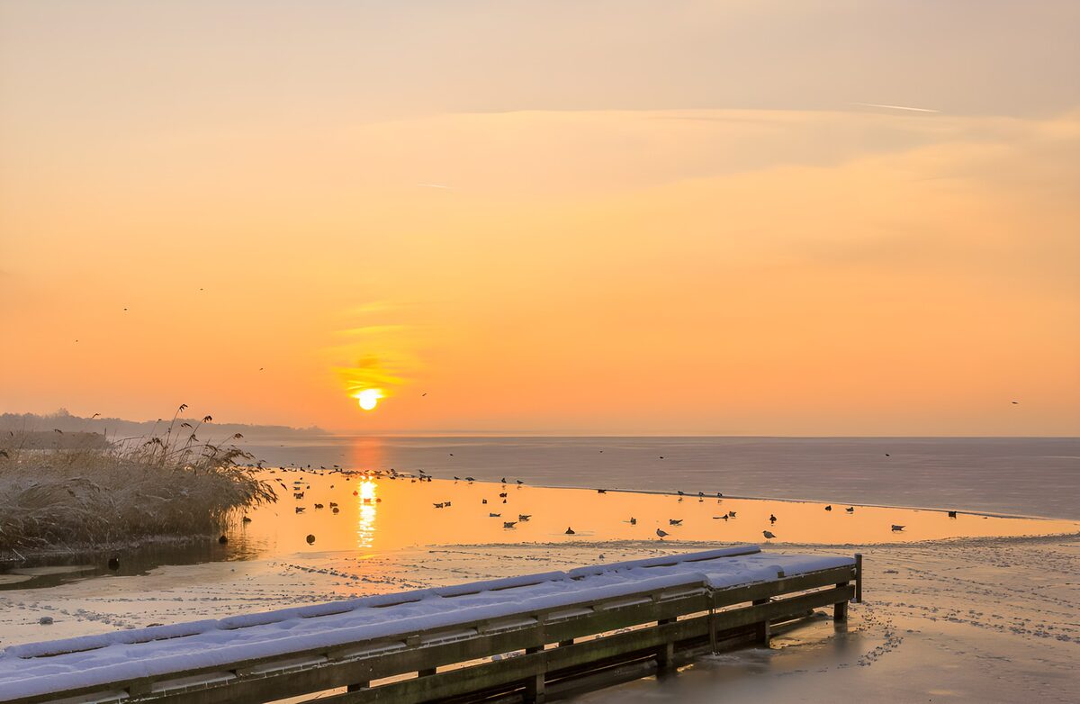 Besneeuwde steiger in meer bij zonsondergang